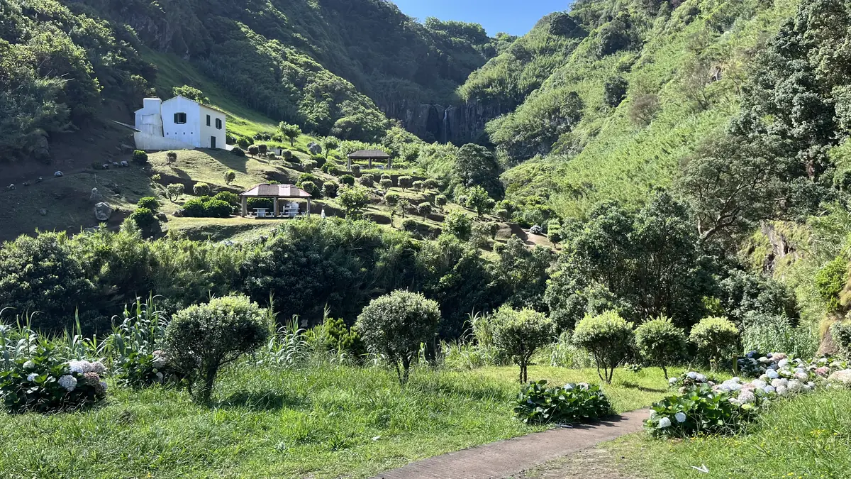 Uma casa branca num vale verde em socalcos, entre colinas arborizadas