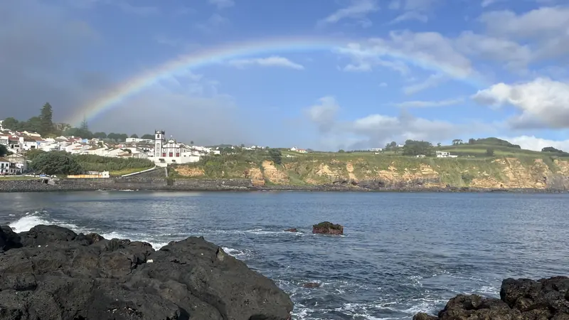 Um arco-íris sobre as rochas vulcânicas negras da costa de São Miguel
