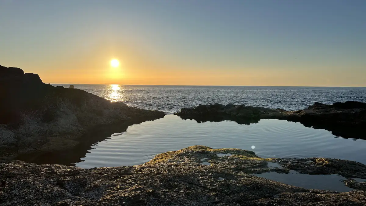 O sol a pôr-se sobre uma piscina natural na costa de São Miguel