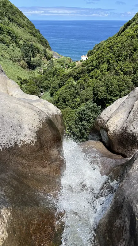 Uma ribeira a correr entre penedos em direção a um vale verde e ao mar