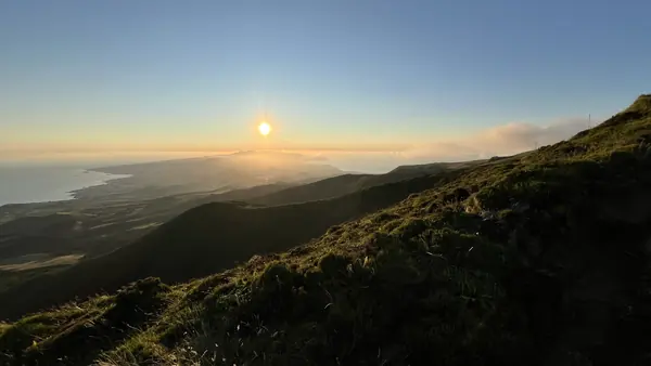 O sol a mergulhar no Atlântico para lá de uma longa crista verde
